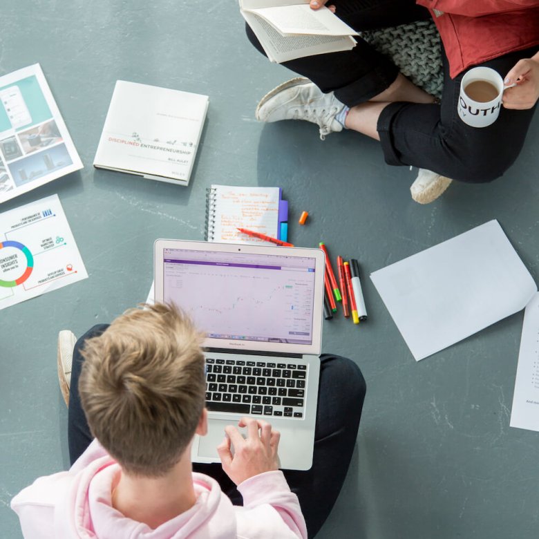 Two Falmouth University students sitting on the floor with a laptop and pieces of paper