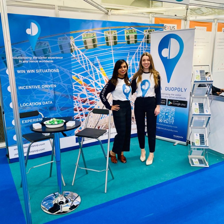 Two women standing together in a blue Data Duopoly exhibition stand