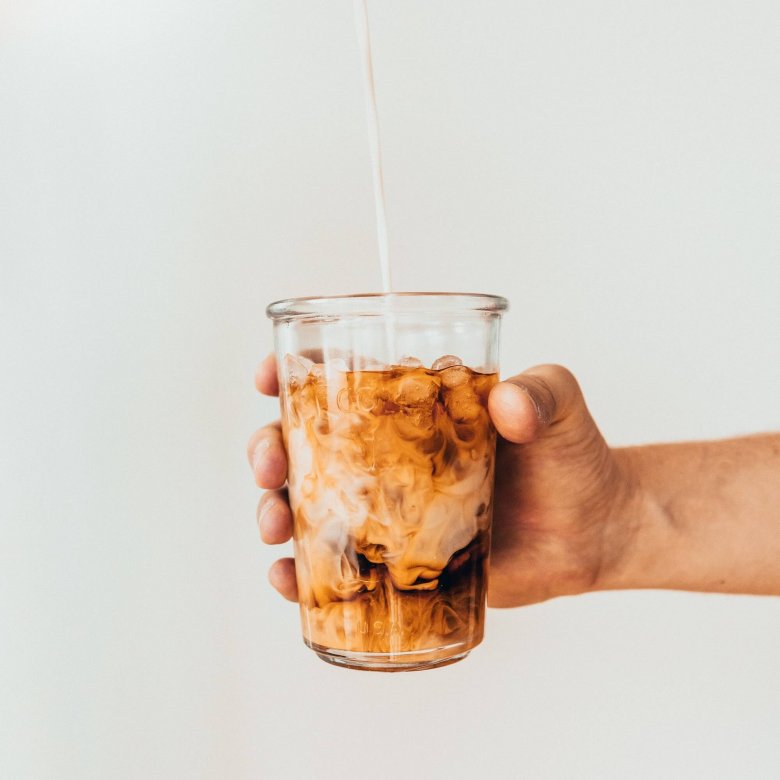 Photo of hand holding out a glass of iced coffee. Photo by Tavis Beck.
