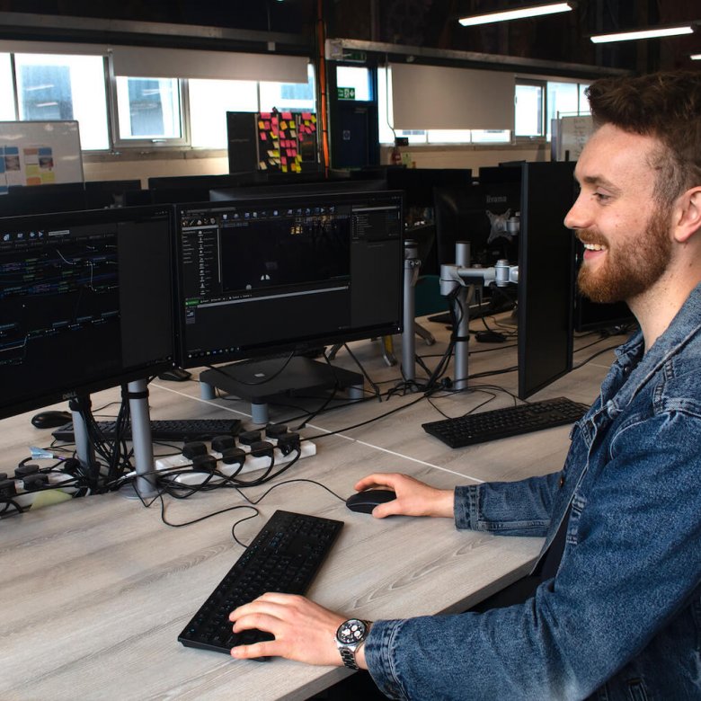 A Falmouth University Games student smiling at a computer screen with a keyboard and mouse