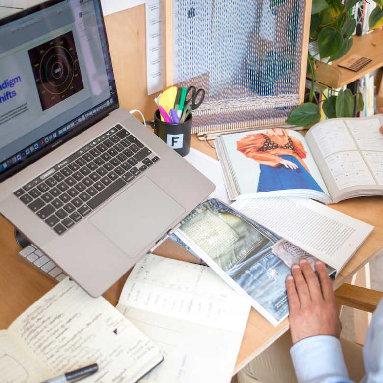 A man sat at a computer with fashion-related books and paper