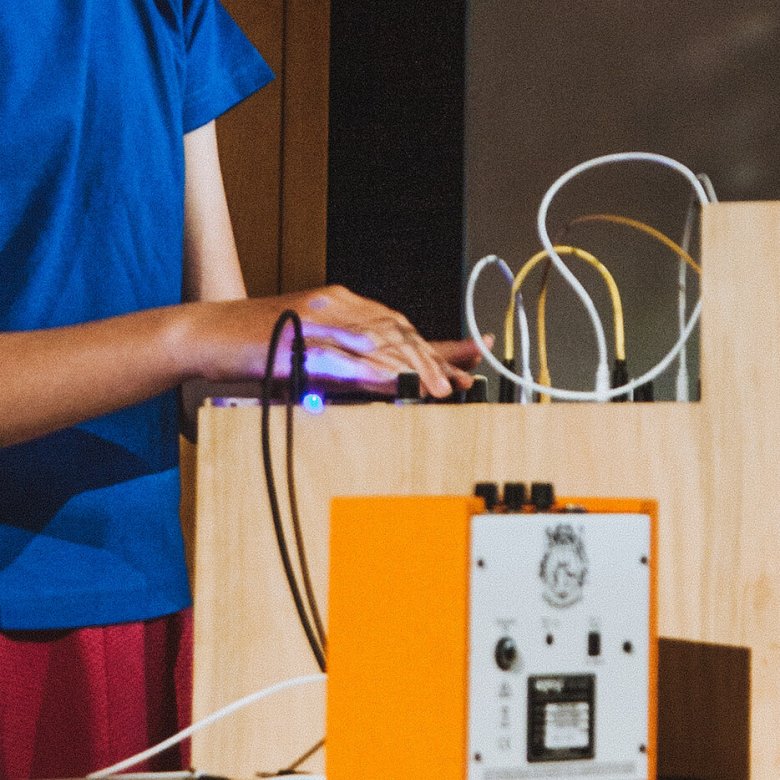 A young person in a blue t-shirt with their hand on a synth