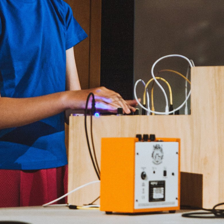 A young person in a blue t-shirt with their hand on a synth