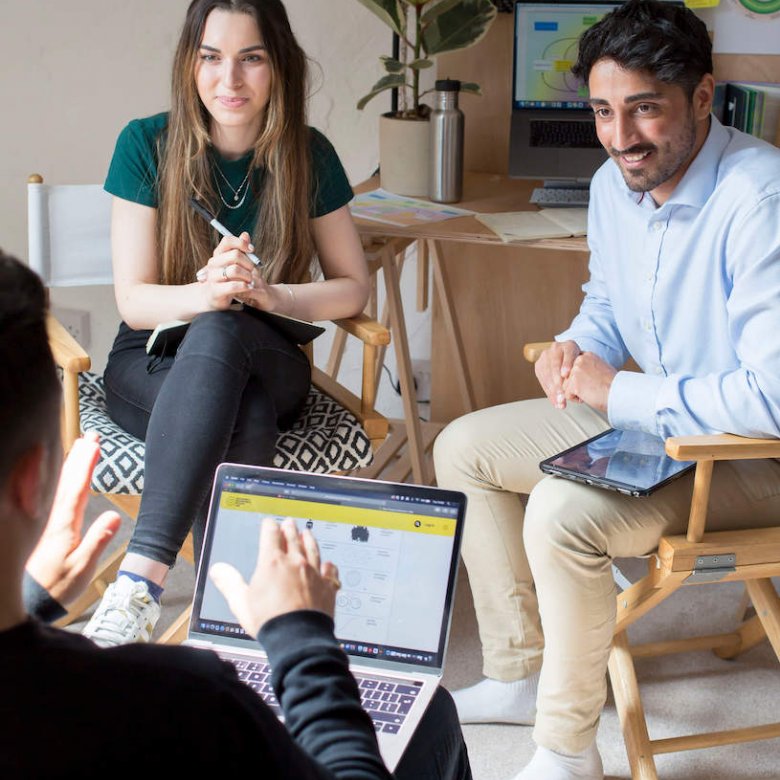 Three people seated in conversation with graphs and a plant in the background