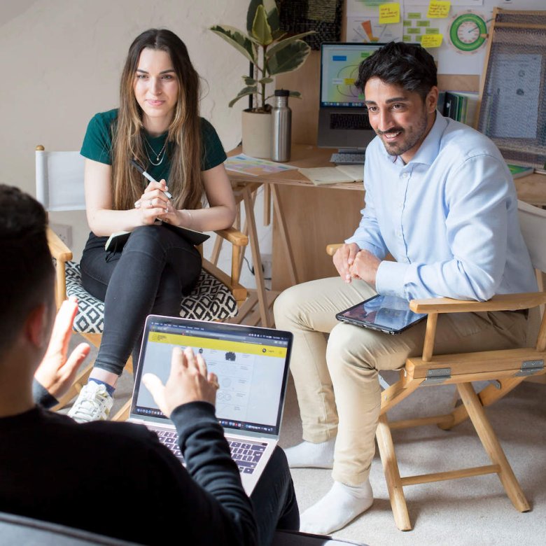 Three people seated in conversation with graphs and a plant in the background