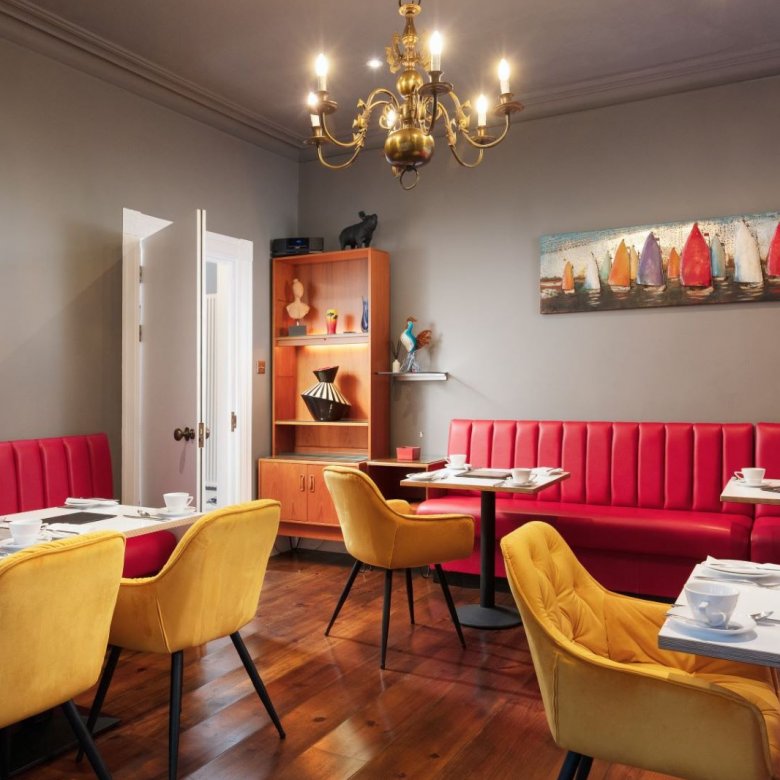 Dining space at Chelsea House in Falmouth. Red booth-style seating, gold chandelier, mustard velvet chairs, wooden flooring 