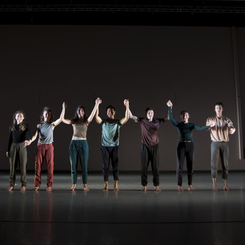 A line of dance students holding hands on a stage