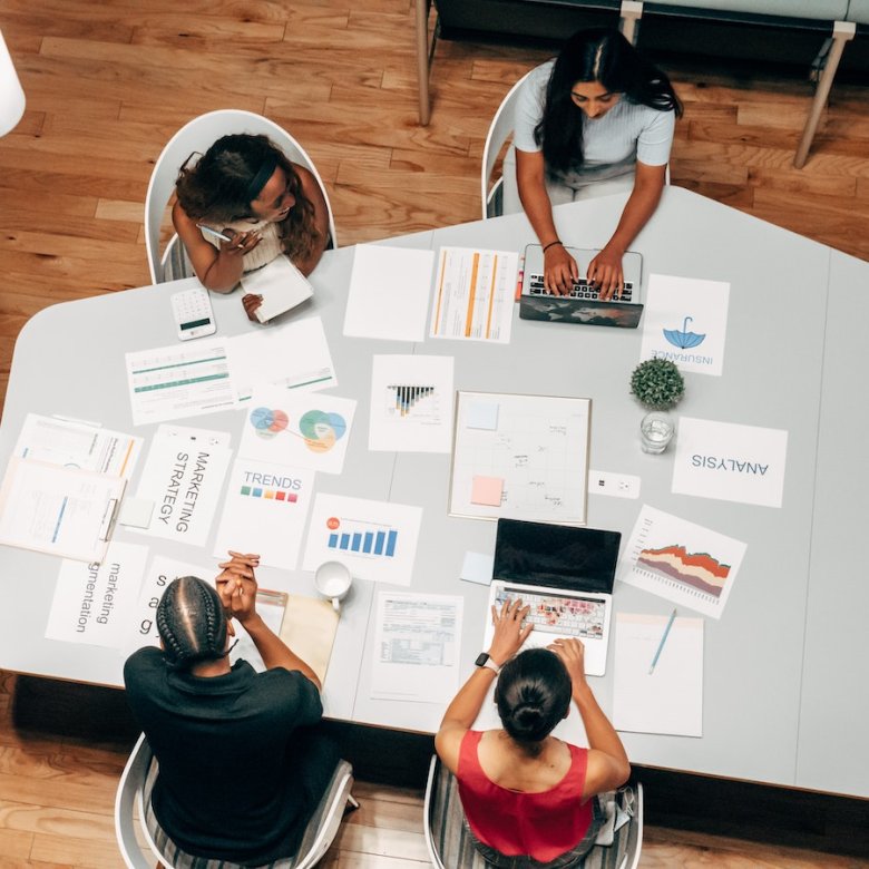 Birds eye view of group of people sat around a table with business strategy papers