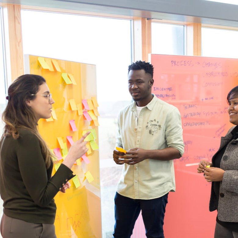 Three people standing in front of a yellow board covered in post-it notes