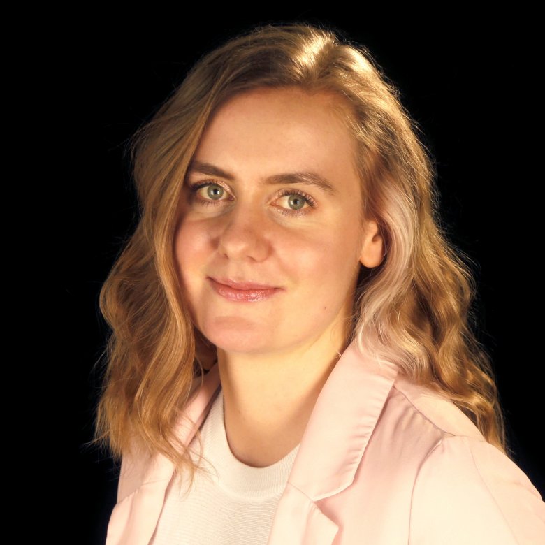 A portrait image of a woman, wearing a pink jacket and a patterned jumper