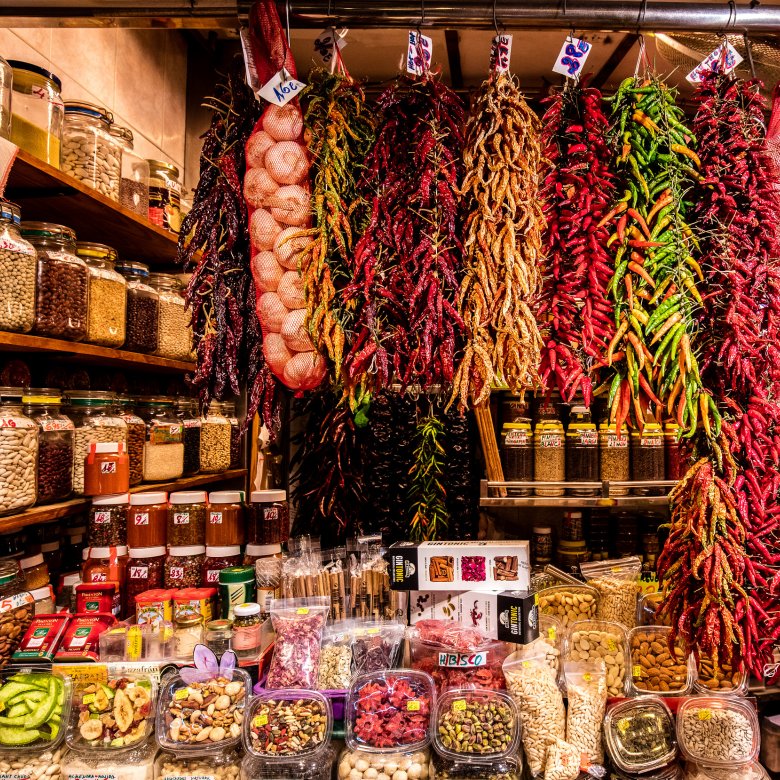 Spices and garlic hang from a market stall, with jars of dried goods surrounding the stall