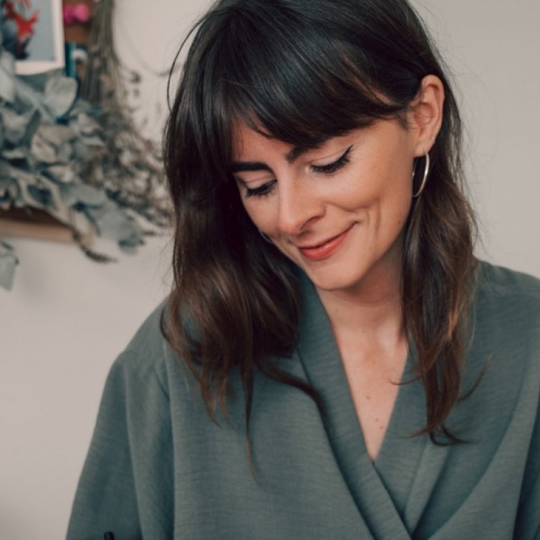 A woman with dark hair looking down and wearing an olive green top