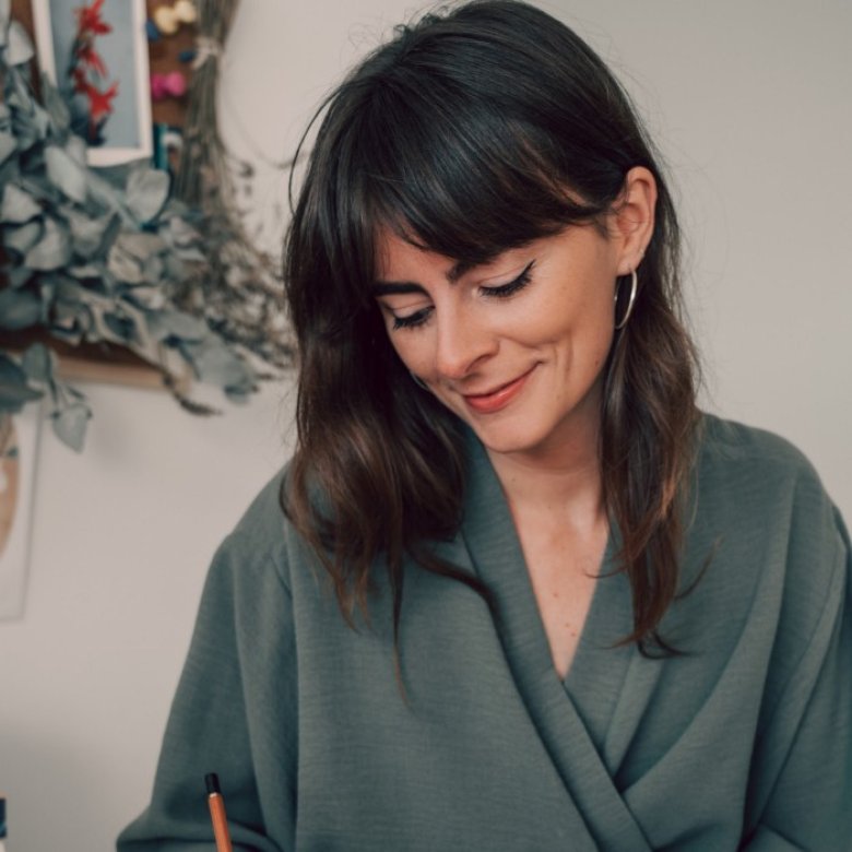 A woman with dark hair looking down and wearing an olive green top