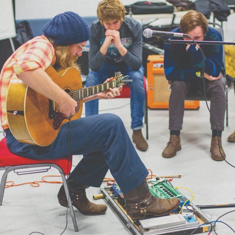 A man plays his guitar in front of three young men