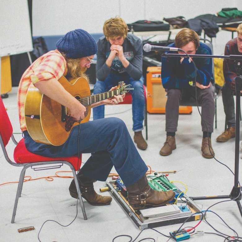 A man plays his guitar in front of three young men