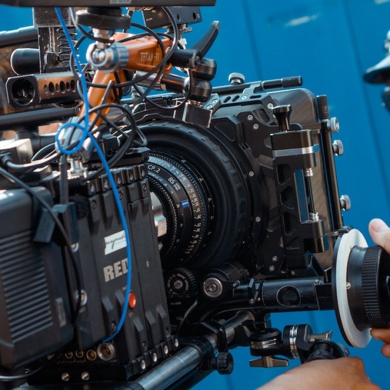 A man controlling a RED camera filming a women wearing sunglasses, a leather hat and jacket