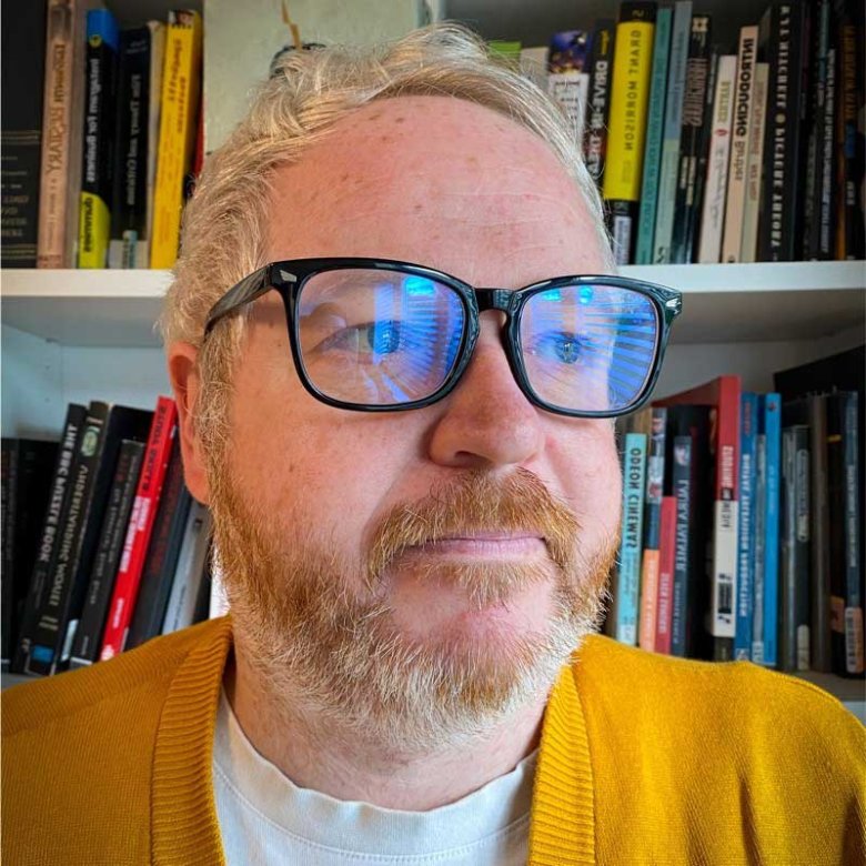 A headshot of Film & TV student Rich Scott smiling wearing glasses and a yellow jumper