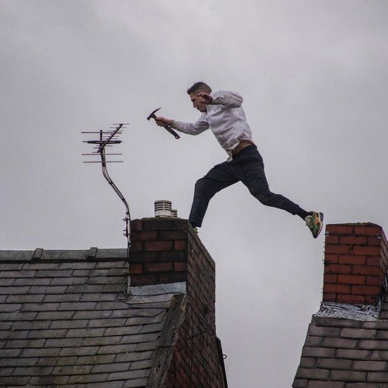 Photo of a man holding a hammer jumping from one rooftop to another during a protest in Manchester. 