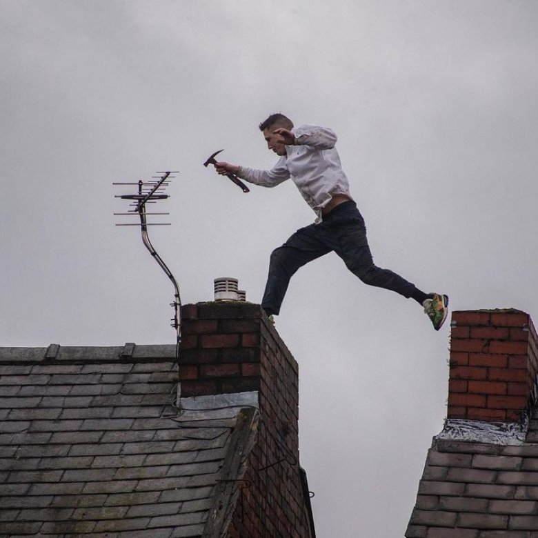 Photo of a man holding a hammer jumping from one rooftop to another during a protest in Manchester.