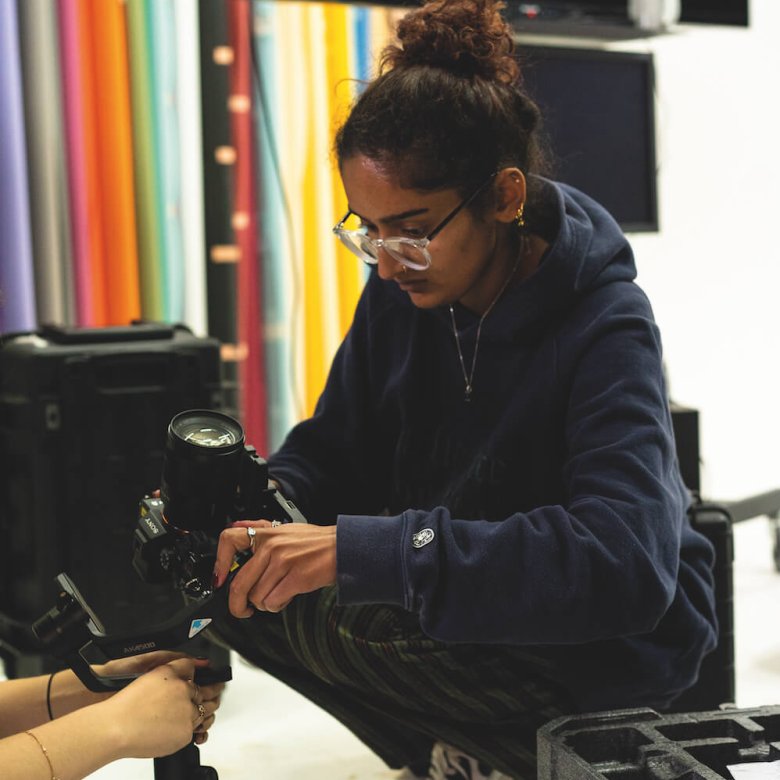 A girl wearing glasses crouched down holding a camera