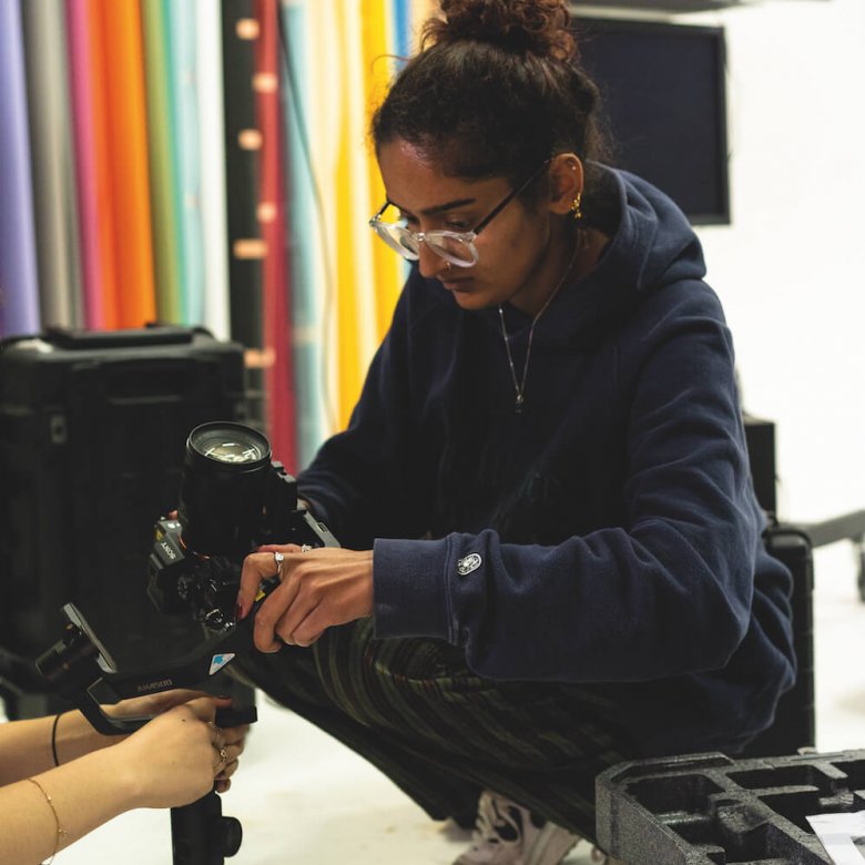 A girl wearing glasses crouched down holding a camera