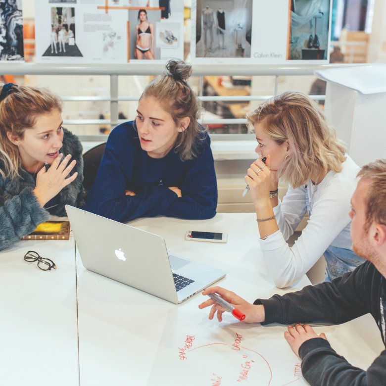 Group of Fashion Marketing students sat talking in front of laptop at Falmouth University