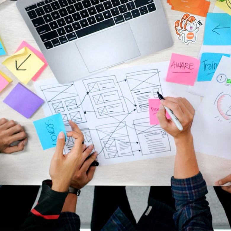 hands sketching a sitemap with a laptop and coloured post-it notes on a table