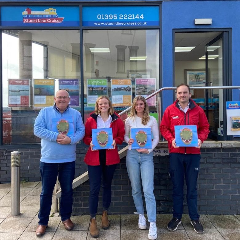 Four people standing outside Stuart Line Cruises shop front, holding a book with a dinosaur on the cover