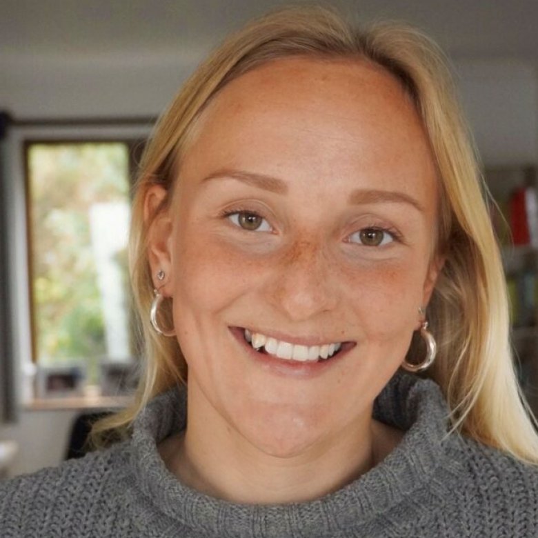 A blonde haired woman wearing a grey jumper smiles 