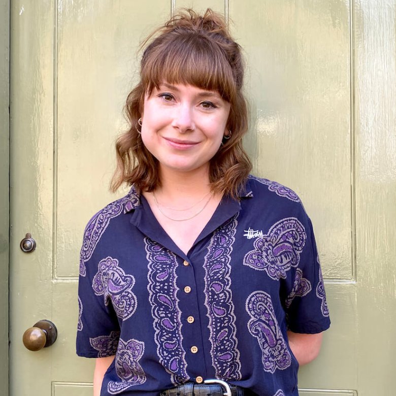 A woman in front of a door wearing a purple shirt