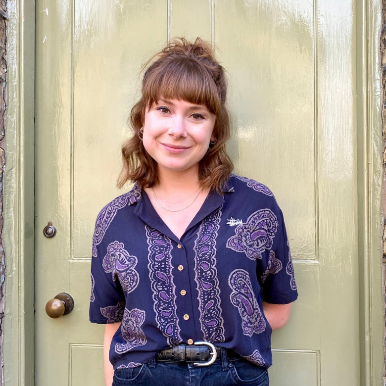 A woman in front of a door wearing a purple shirt