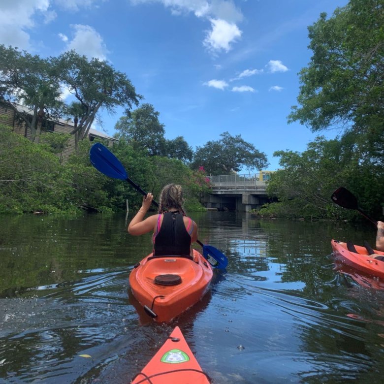 A girl in an orange kayak on the water with trees