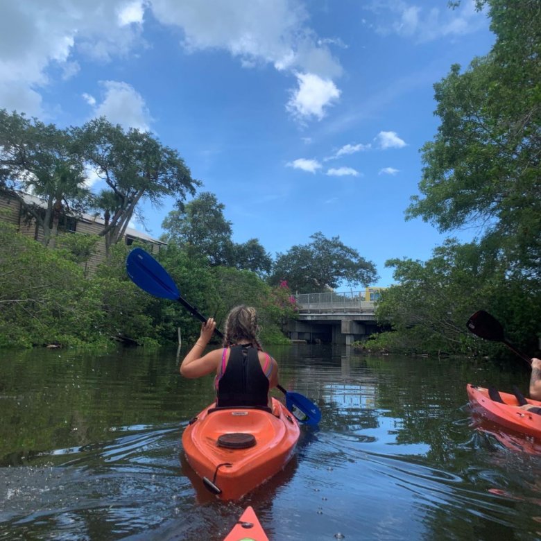 A girl in an orange kayak on the water with trees