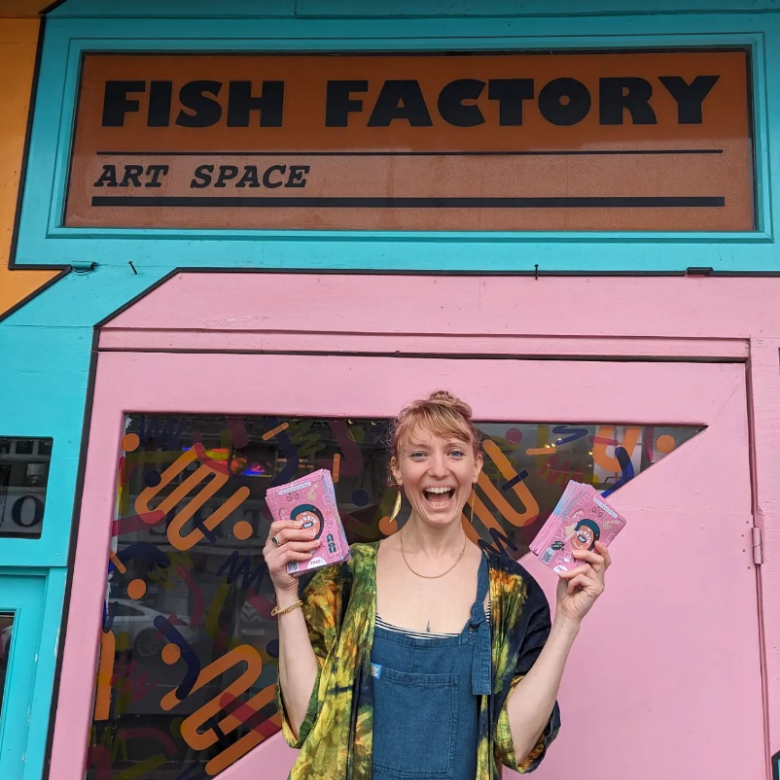 A woman stood outside a pink building holding maps