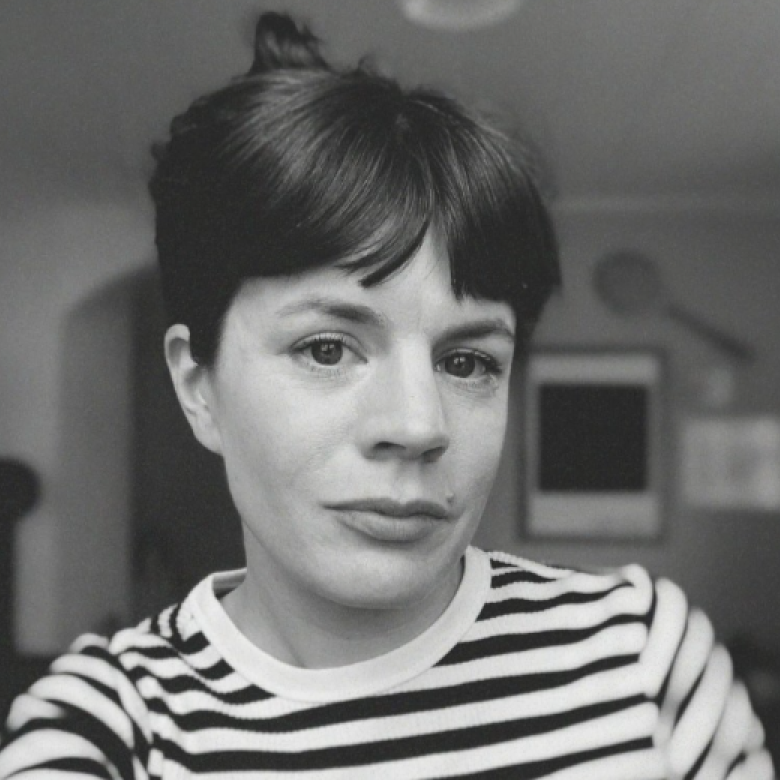 A woman with dark hair wearing a stripy top looking into the camera