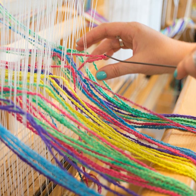 A hand using a weaving machine with multi-coloured wool