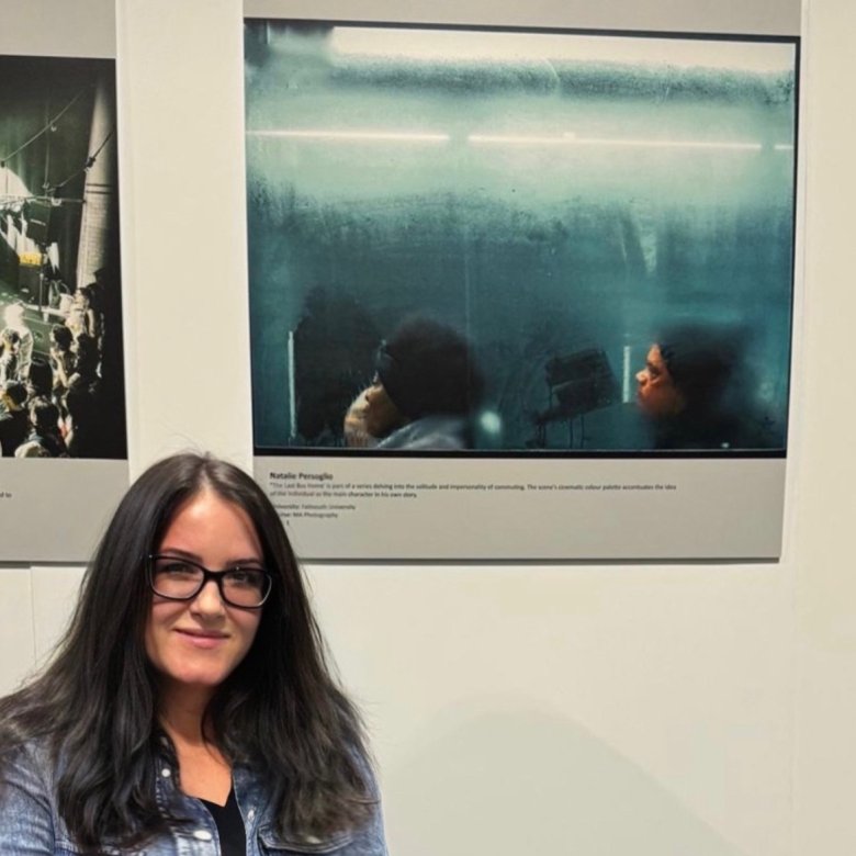 Photography student Natalie Persoglio standing next to her award-winning image of two people on a bus