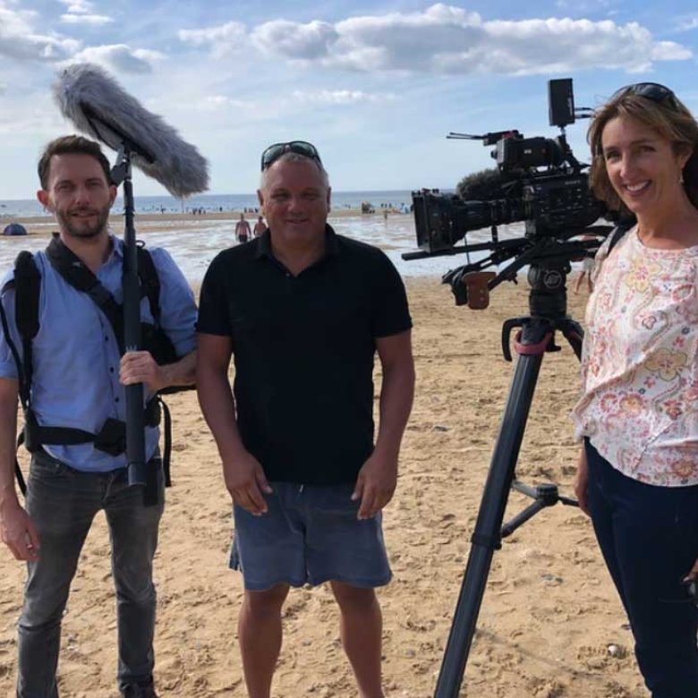 Three people stood on a beach with cameras and filming equipment