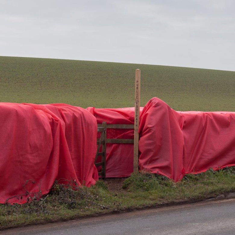 Large red material draped over a wooden fence with a public footpath sign