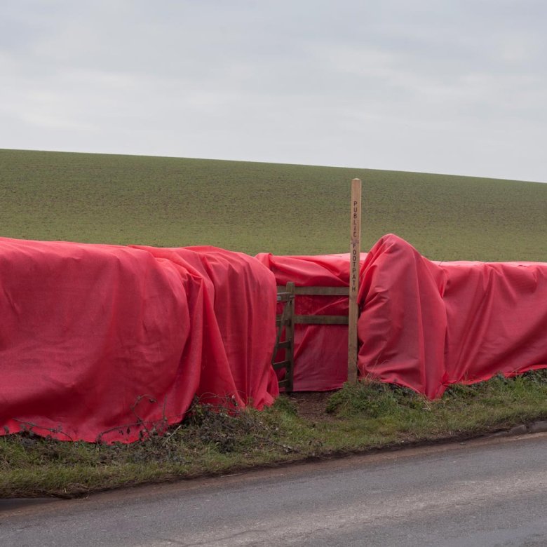 Large red material draped over a wooden fence with a public footpath sign