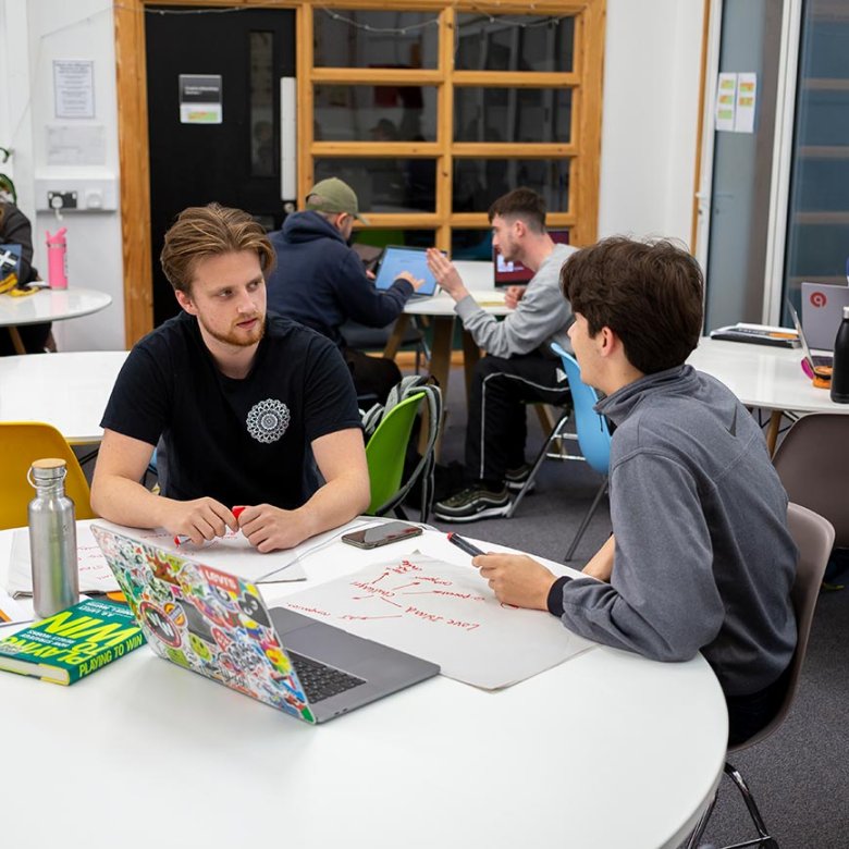 Two male Creative advertising students engaged in conversation at a table