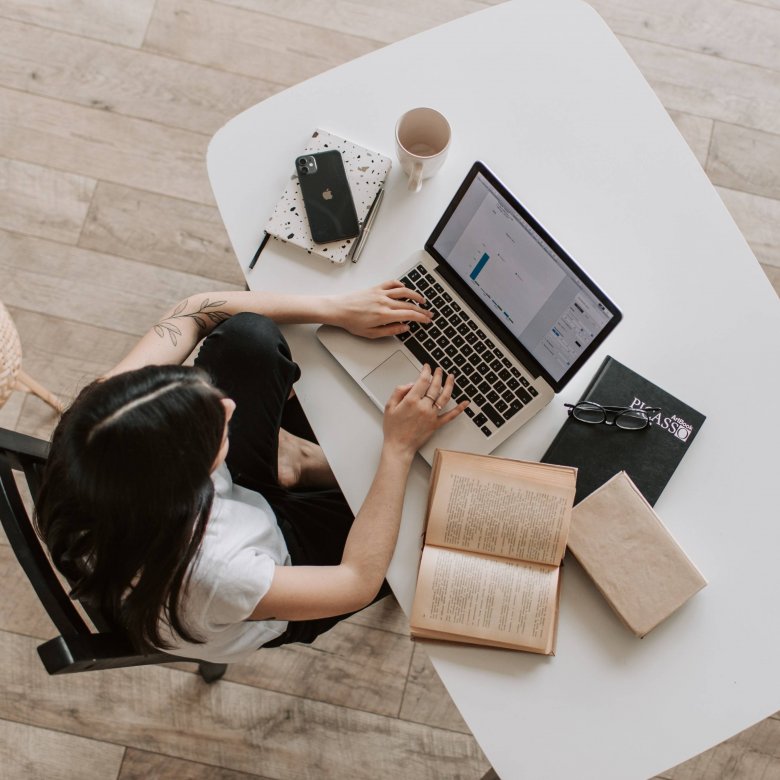 A birds eye view shot of a woman sitting at a desk with laptop and notepad