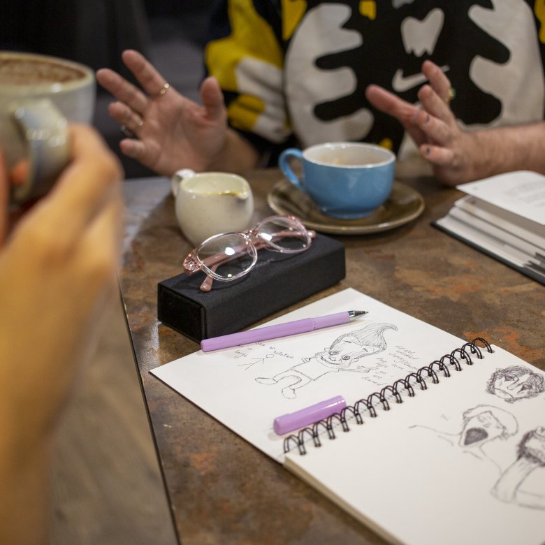 A photo of two students drinking coffee with drawings on the table