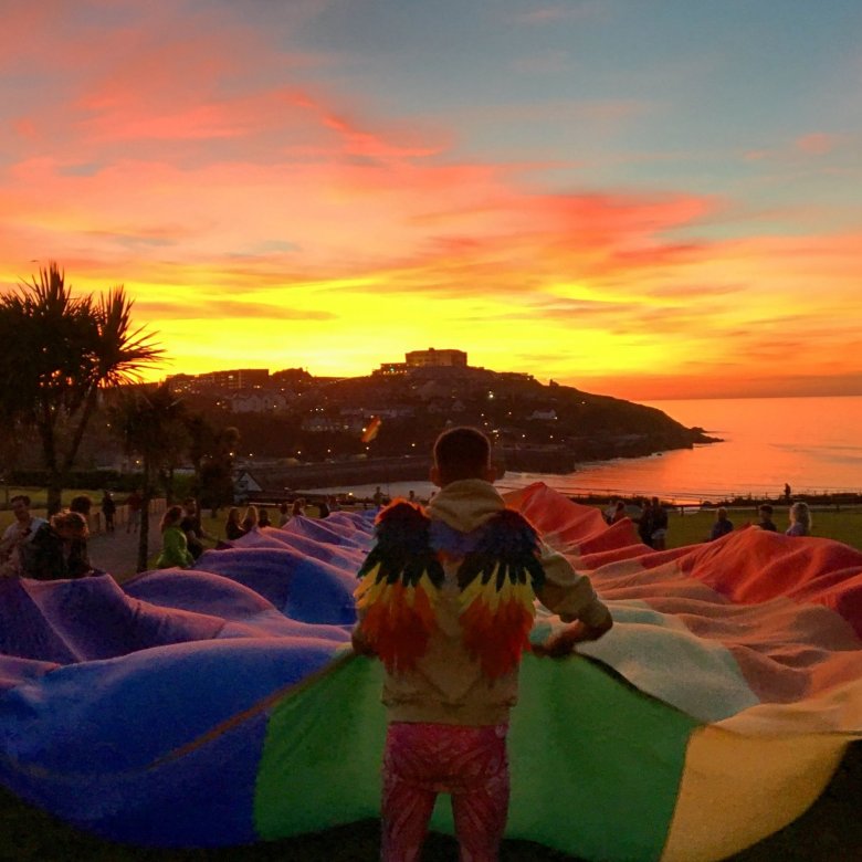 A large rainbow flag is held aloft at sunset