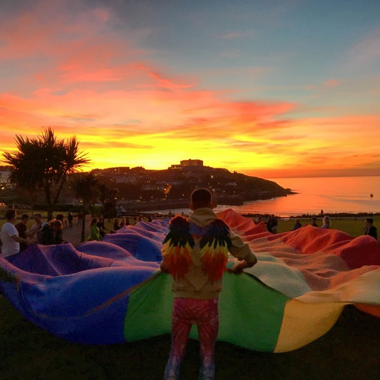 A large rainbow flag is held aloft at sunset