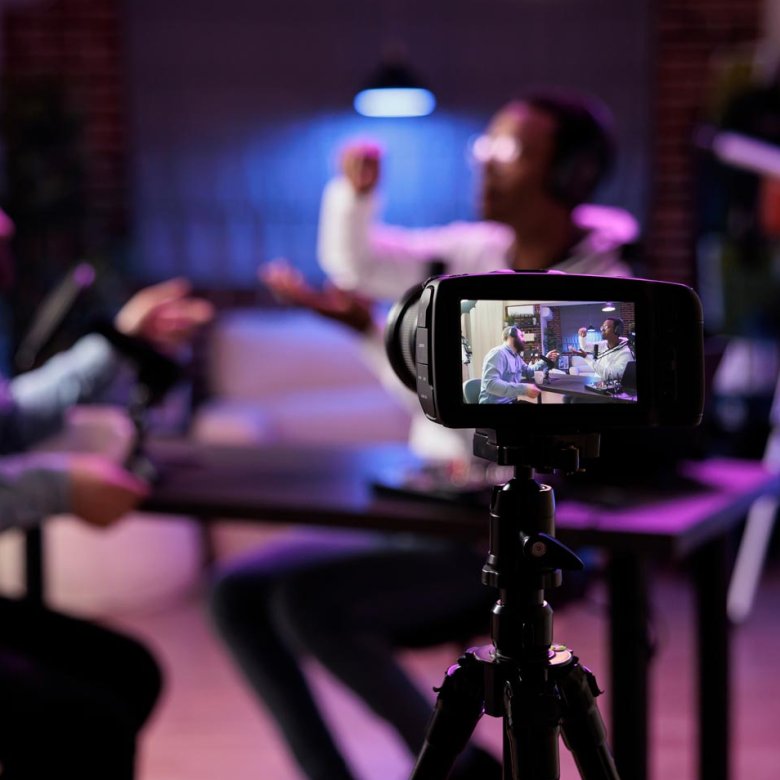 View of SLR camera filming two people in conversation around a table