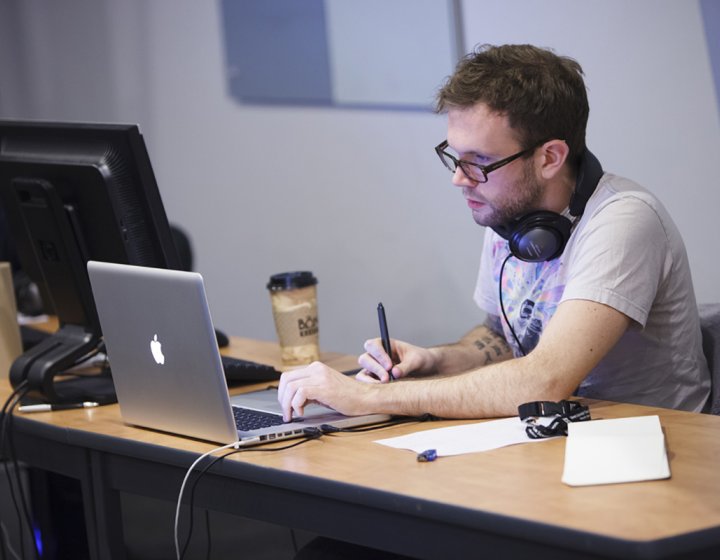 Student with earphones around neck working on graphics tablet.