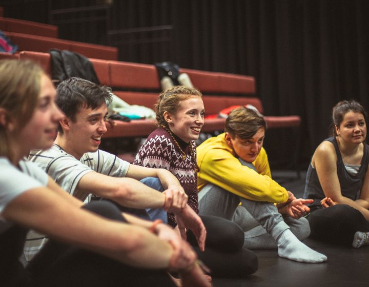 Group of students sat on theatre floor and smiling.