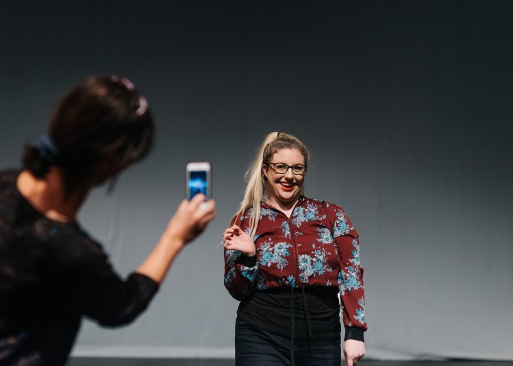 A student smiling while being filmed on a phone by another student