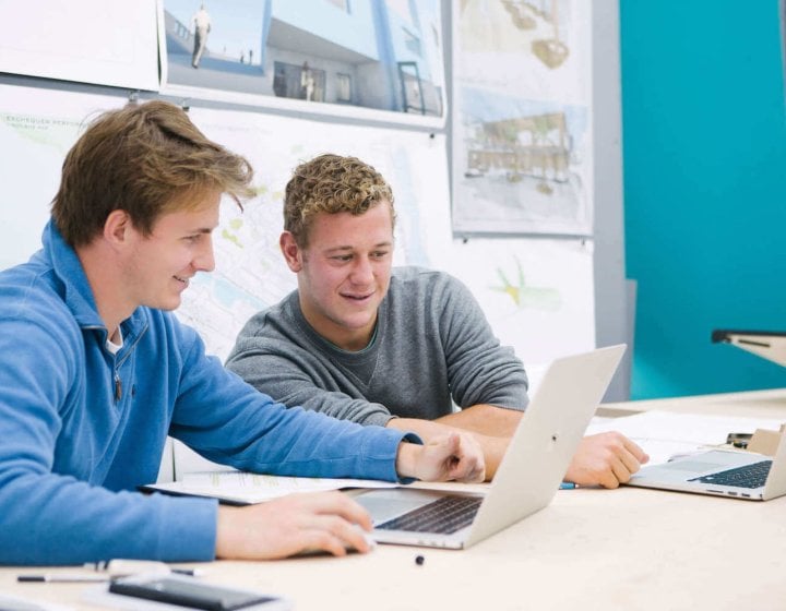 Two male students seated while looking at a laptop